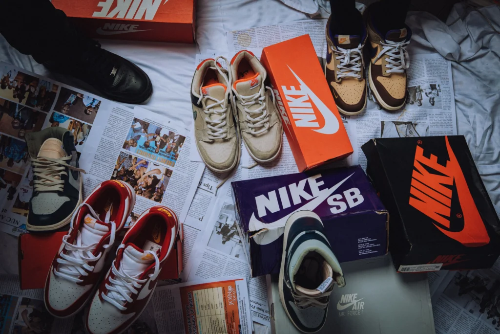 Collection of Nike trainers and shoeboxes arranged across magazines and newspapers on a bed, showcasing different sneaker styles in an editorial flat lay that reflects sneaker collecting and streetwear culture.