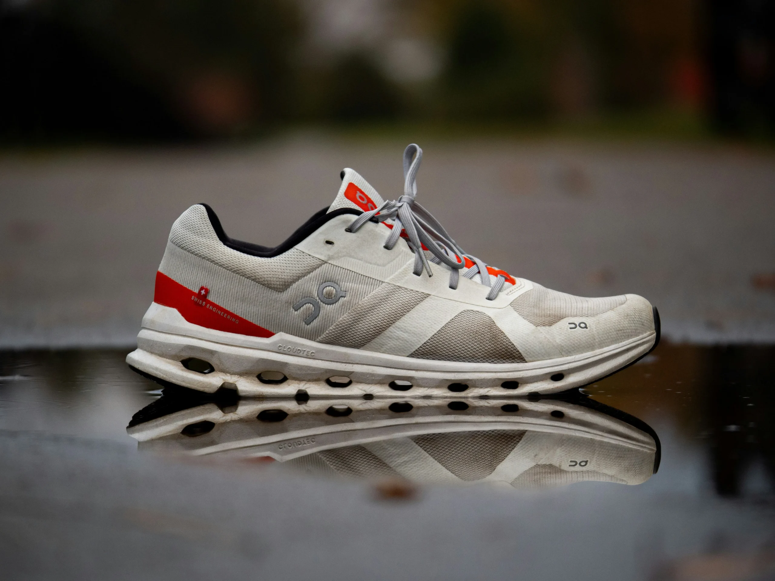 White and red On running shoe reflected on a glossy surface.