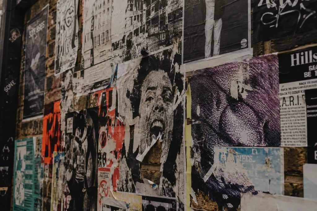 What Is Culture Marketing? (and Why Most Brands Get It Wrong) Close-up of a weathered brick wall covered with layered gig posters, community notices, independent event flyers and torn magazine-style artwork, showing faded paper textures, overlapping graphics and the accumulated character of an urban cultural space.