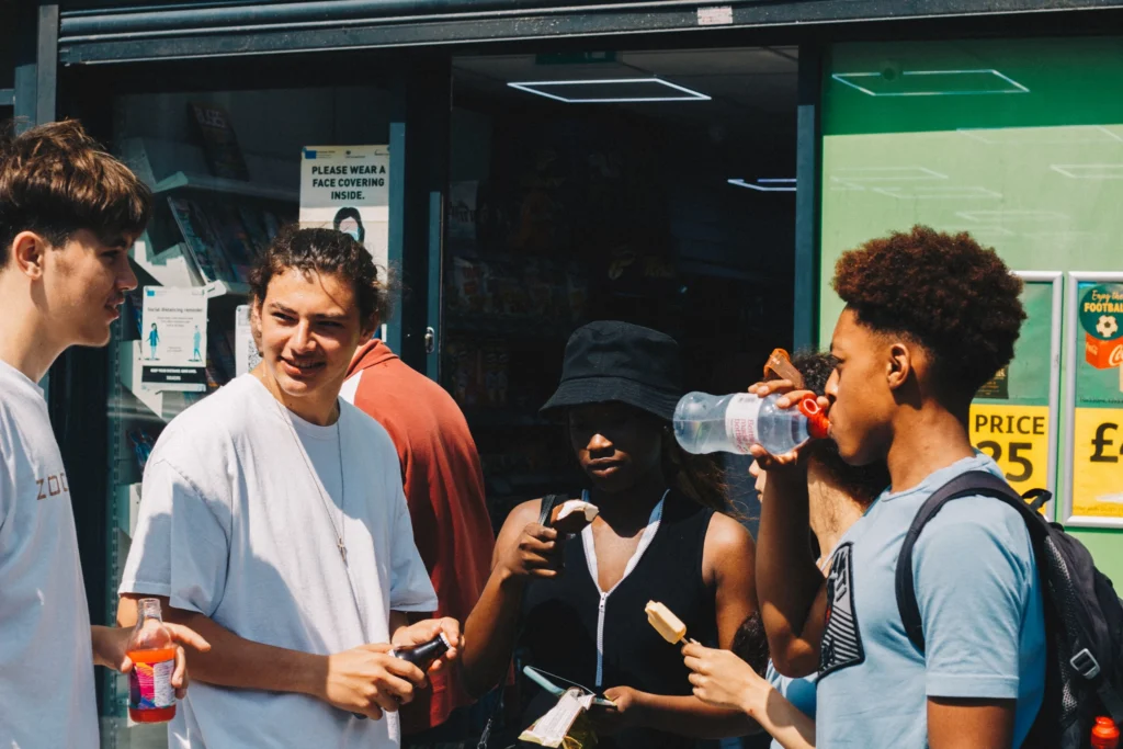 Youth Subcultures: What They Are and How to Identify Them Group of young people outside a local corner shop on a hot day, sharing drinks and ice lollies, showing the place-based scenes that shape youth culture